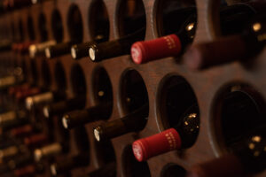 Close-up of wine bottles stored horizontally in a dark wooden wine rack, with visible red and black caps.